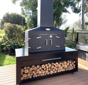 Engel Fire positioned on a backyard deck with stacked firewood storage below.